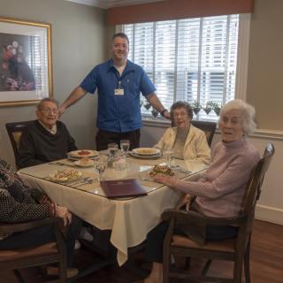 Elderly individuals dining together with a caregiver in a cozy setting.