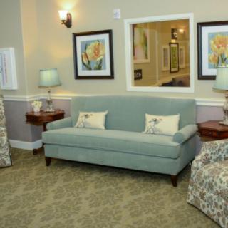 A cozy living room with a blue sofa, lamps, and floral artwork.