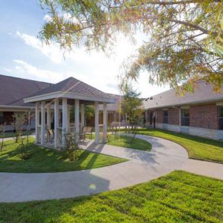 A sunny courtyard with a curved pathway and well-maintained landscaping surrounded by buildings.