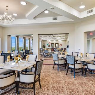 An elegant dining room with tables and chairs, featuring chandeliers and large windows.