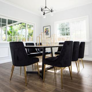 A modern dining room with a sleek table and black chairs, featuring large windows and a stylish chandelier.