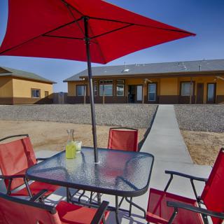 A patio area with a red umbrella and chairs set around a glass table, overlooking a house and backyard.