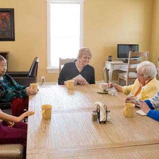 A group of seniors enjoying coffee and conversation at a table in a community setting.