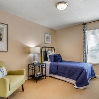 A cozy bedroom featuring a single bed with blue bedding, an armchair, and decorative wall art.