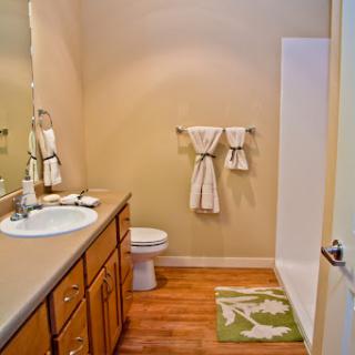 A well-organized bathroom featuring a sink, toilet, and shower area, complemented by neatly arranged towels and a decorative mat.