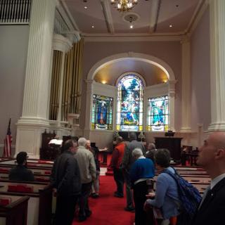 A gathering of people inside a church, showcasing beautiful stained glass windows and classic architectural elements.