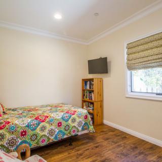 A cozy bedroom featuring a single bed with a colorful bedspread, a small bookshelf, and a wall-mounted television.