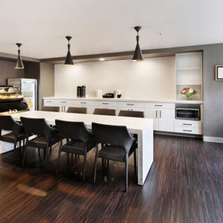 A modern kitchen with sleek white countertops, bar stools, and pendant lighting.