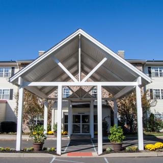 A front view of a building entrance with a large, white triangular awning supported by columns.
