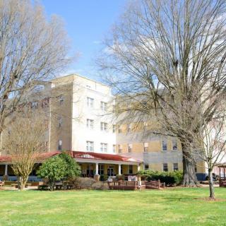 A multi-story building surrounded by trees and grass on a clear day.