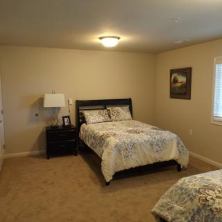A cozy bedroom with a double bed, nightstand, and lamp, featuring neutral decor and carpet flooring.