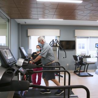 A healthcare worker assists an elderly person on a treadmill in a gym setting.