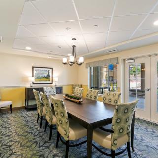 A well-lit dining or conference room with a long wooden table surrounded by chairs and adorned with a chandelier and decorative wall art.