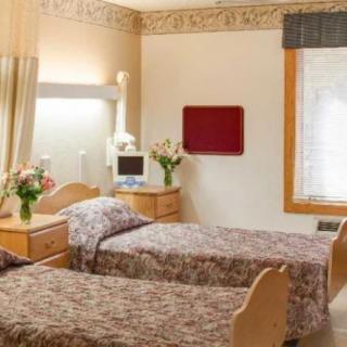 A well-lit hospital room with two twin beds, decorated with floral arrangements and equipped with medical devices.