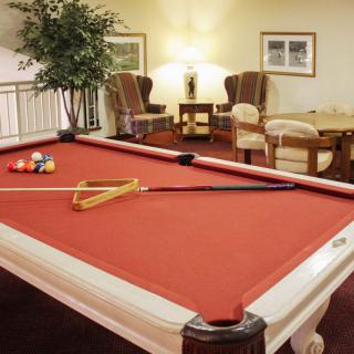 A cozy game room featuring a red-felt pool table with cues and billiard balls ready for play.