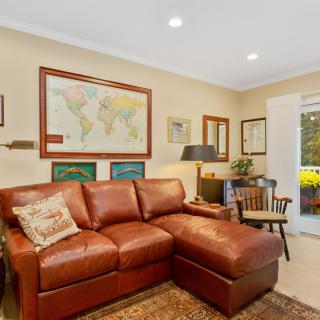 A cozy living room with a leather couch, world map, and various artworks on the walls.