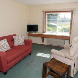 A cozy living room with a red sofa, armchair, small TV, and a window view.