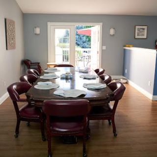 A well-lit dining room with a large table surrounded by chairs, featuring hardwood flooring.