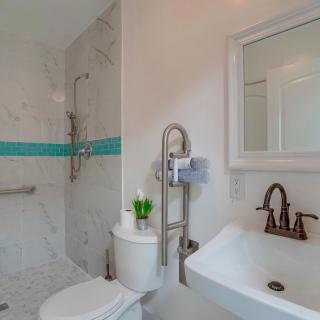A modern bathroom featuring a shower with white and turquoise tiles, a toilet, and a sink with a mirror above it.