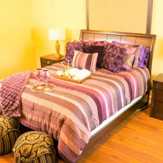 A cozy bedroom with a colorful striped bedspread, decorative pillows, and wooden furniture.