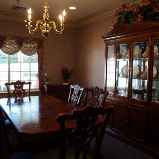 A traditional dining room with a wooden table and chairs, a chandelier, and a display cabinet near the window.