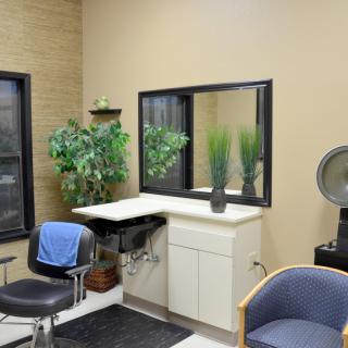 A cozy hair salon interior featuring a styling station with a mirror, sink, and salon chair, accented by decorative plants and additional seating.