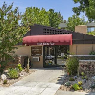 Entrance to a building with a red awning and landscaped surroundings.