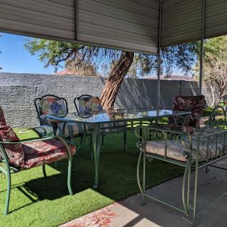 A cozy outdoor patio area with a glass table and cushioned chairs under a shaded canopy.