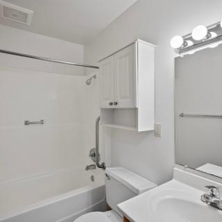 A clean, minimalist bathroom featuring a shower, toilet, and sink with modern lighting.