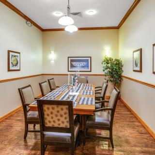 A well-lit dining room with a long table surrounded by chairs, featuring wall artwork and a decorative plant.