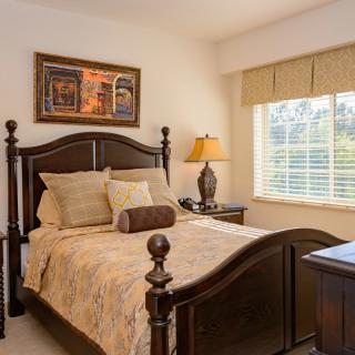 A cozy bedroom featuring a wooden bed, decorative pillows, and a bedside lamp near a window.
