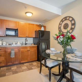 A cozy kitchen and dining area featuring a small dining table with flowers, wooden cabinets, and a large wall clock.