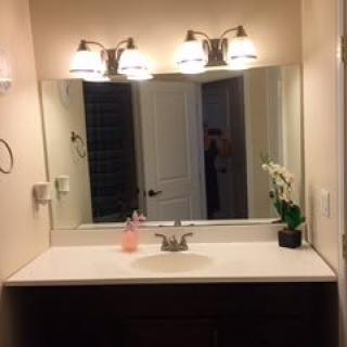 A bathroom vanity with a large mirror, bright lighting, and decorative orchid.