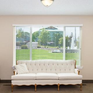 A cozy living room with a white sofa and large windows featuring blinds.