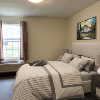 A cozy bedroom with a neatly made bed, featuring neutral-colored bedding and a painting on the wall.