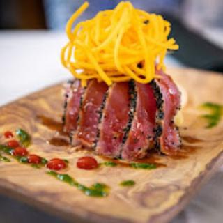 A beautifully plated dish featuring seared tuna topped with crispy noodles and drizzled with vibrant sauces.