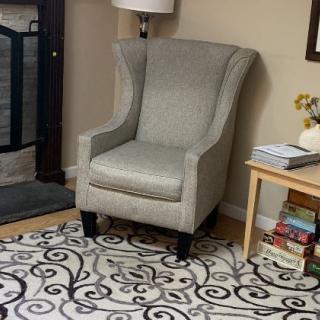 A cozy living room corner with an armchair, patterned rug, and a side table with books.