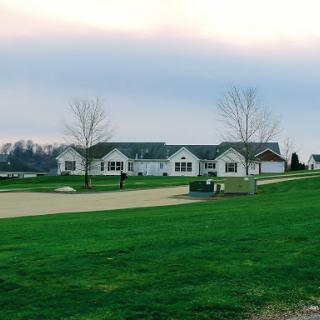 A picturesque rural scene featuring a large house surrounded by green grass and trees under a cloudy sky.