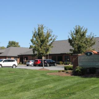 A view of a well-maintained building with lush landscaping and parked cars on a sunny day.