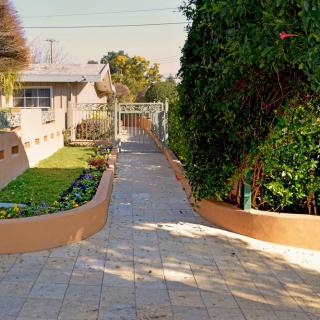 A landscaped pathway bordered by garden areas and trees, leading to a house.