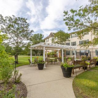 A scenic outdoor patio area with a pergola, surrounded by greenery and trees.