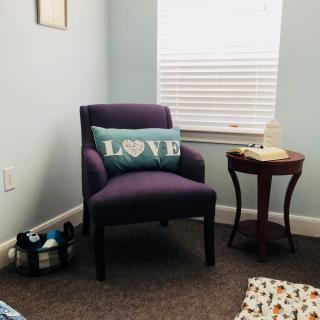 A cozy living room corner featuring a purple chair with a 'LOVE' pillow and a small side table.