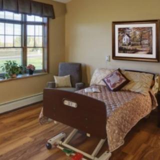 A well-lit healthcare room featuring a hospital bed, an armchair, and a window with a scenic view.