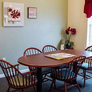 A cozy dining area with a wooden table surrounded by chairs, adorned with wall art and a window with red curtains.