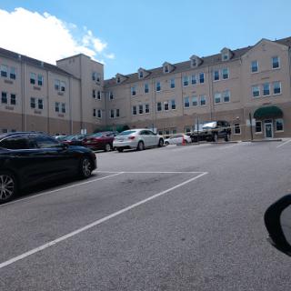 A view of a multi-story building with a parking lot filled with vehicles under a partly cloudy sky.
