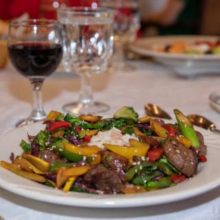 A gourmet dinner featuring a colorful vegetable and steak dish paired with a glass of red wine.