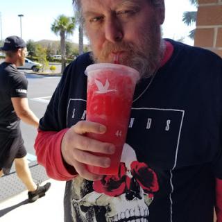 A man enjoying a large red beverage outside.