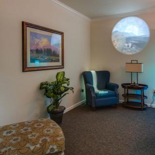 A cozy living room with an armchair, lamp, plant, and artwork on the wall.