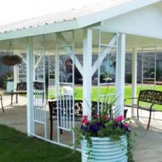 A charming outdoor seating area with a pergola, decorated with flower planters and surrounded by a lush green lawn.