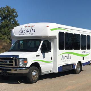 A white Arcadia shuttle bus parked outside on a sunny day.